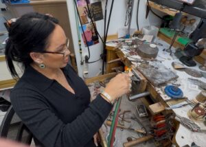 A woman crafting glass art using a torch in a workshop.