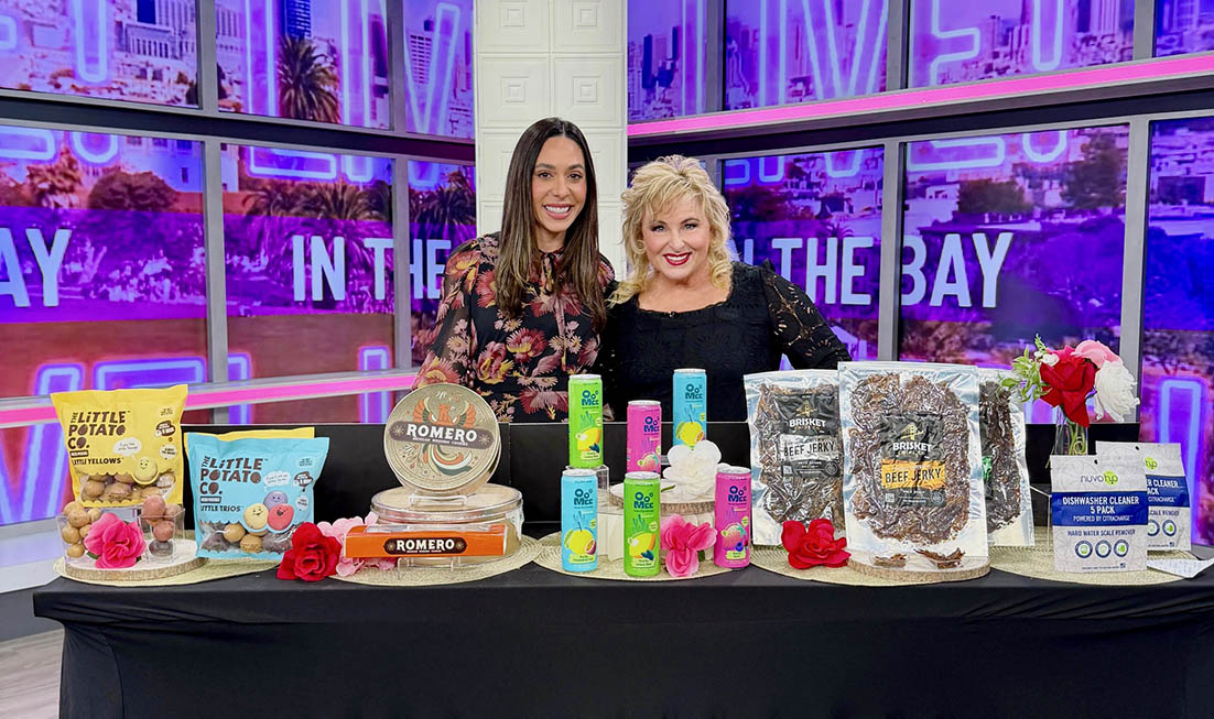 Two women showcasing colorful products on a TV set with vibrant purple lighting.