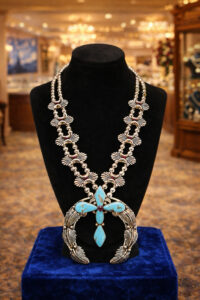 Intricately designed turquoise and silver necklace displayed on a black bust.
